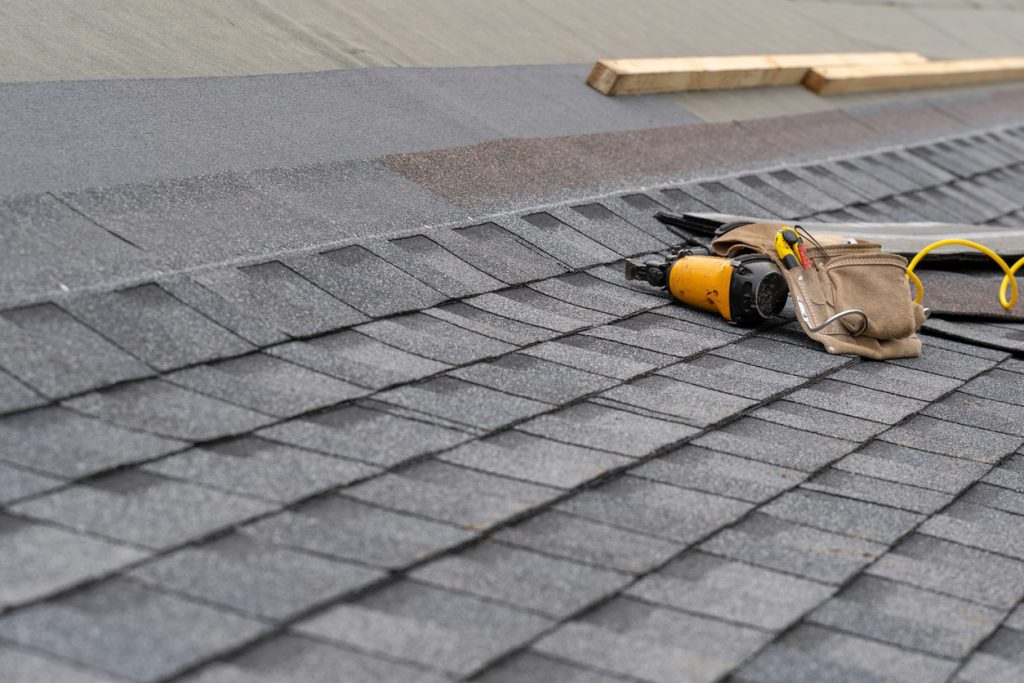 A close-up view of a damaged asphalt shingle on a roof. The shingle is cracked and worn out, showing signs of wear and tear.