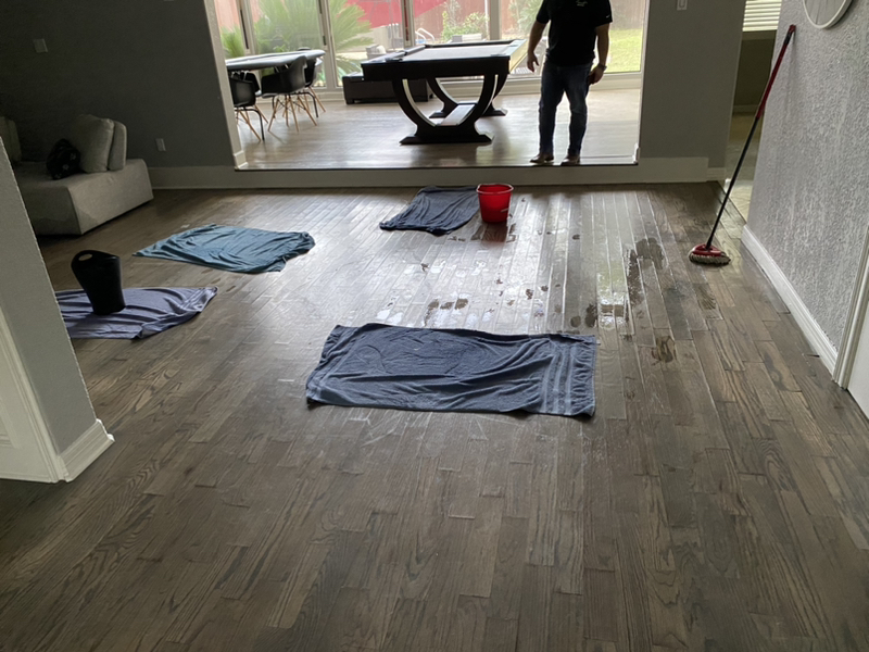 The photo shows a flooded room with water pooling on the floor, causing visible damage to walls, furniture, and belongings.